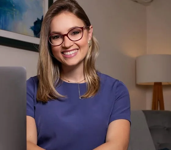 Aline Sá Copetti sorrindo no consultório, com quadro azul ao fundo